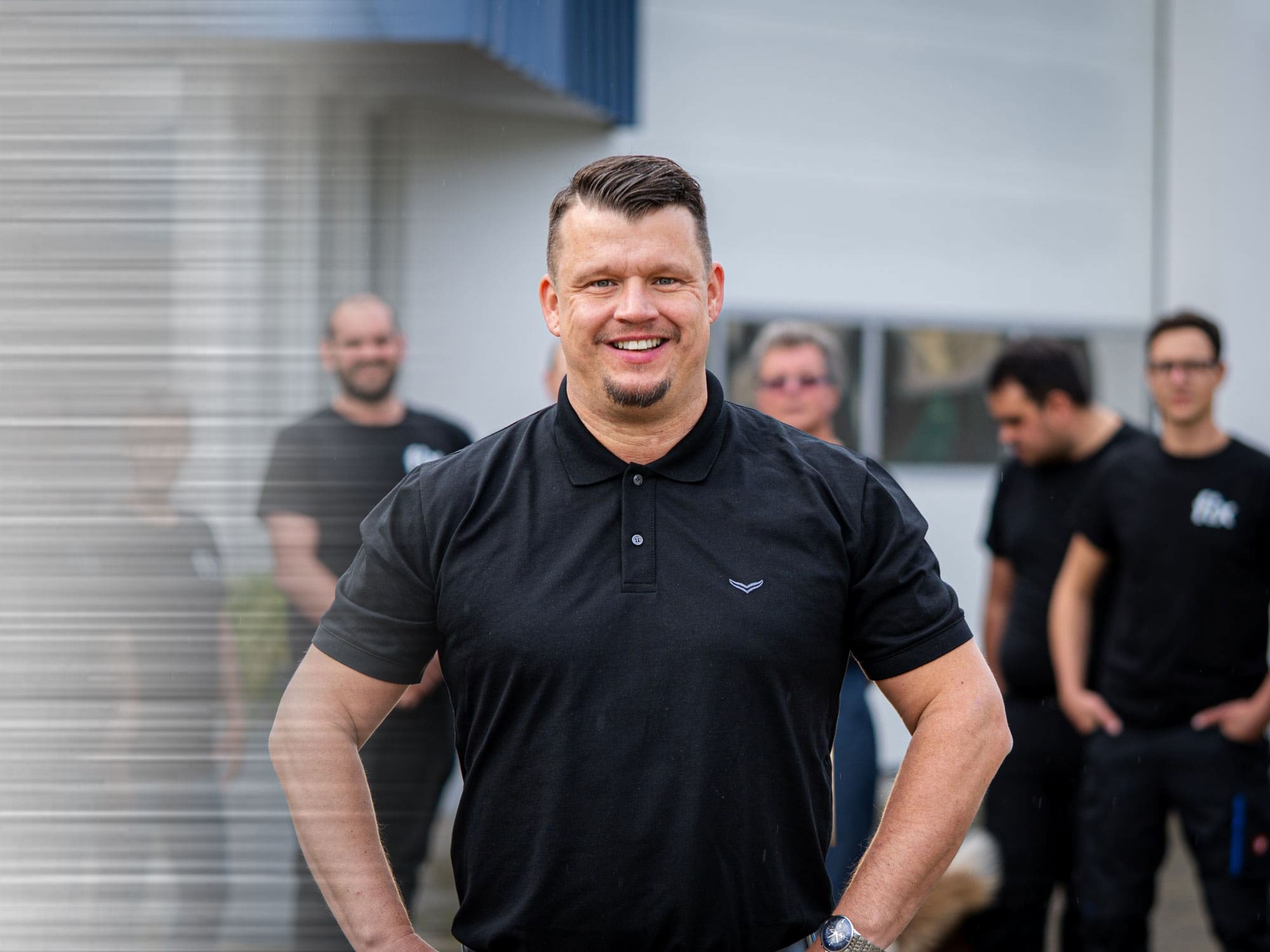 Dominik Fix vor der Fertigungshalle der Fix CNC Koordinaten-Schleiftechnik, im Hintergrund Teile der Belegschaft.
